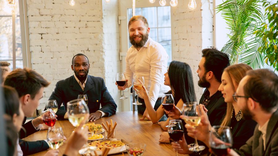 En gruppe af personer er samlet og drikker vin og spiser mad, og det ser ud til, at de holder fest.