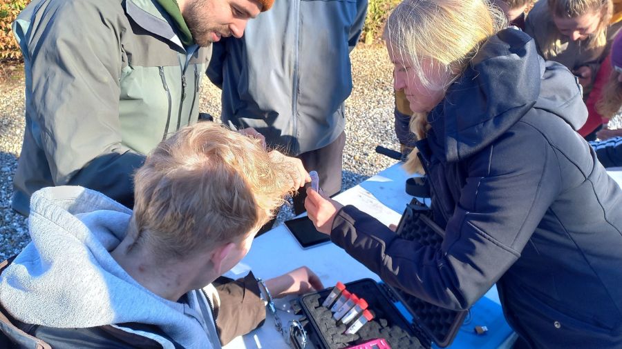 Billedet viser en teambuilding aktivitet, Escape Game, hvor deltagerne arbejder tæt sammen udendørs for at løse gåder og opgaver ved et bord fyldt med redskaber og materialer. Stemningen er fokuseret og samarbejdsorienteret, hvilket styrker teamets evne til at arbejde effektivt sammen.