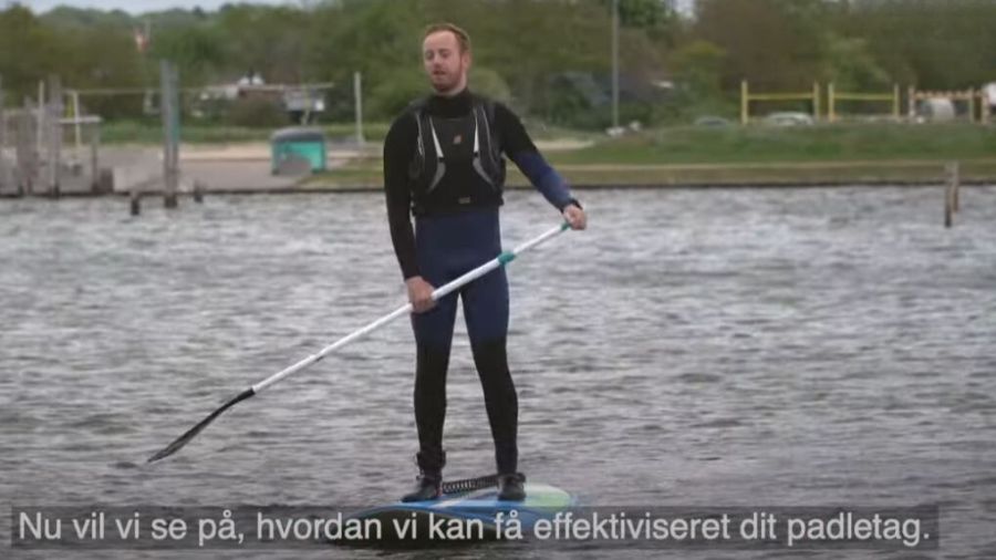 På billedet ser vi en person stående på et paddleboard på vandet, hvilket er en form for vandsport. Han er iført en våddragt og holder en paddel, mens han balancerer på boardet