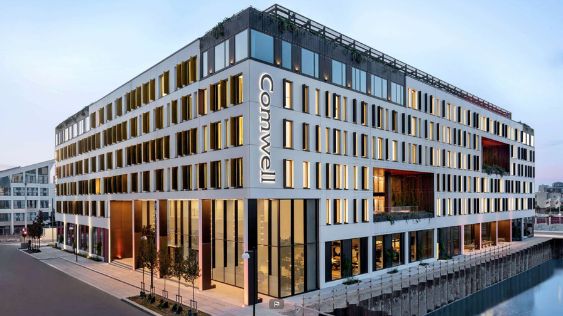 Billedet viser det kendte Comwell Hotel i København, hvor navnet "Comwell" tydeligt ses på facaden. Hotellet har en stilfuld arkitektur med rene linjer og store vinduer, der giver et indblik i den livlige atmosfære indendørs. Dets elegante design og sofistikerede udstråling gør det til en populær destination for konferencer og møder i et større byområde.