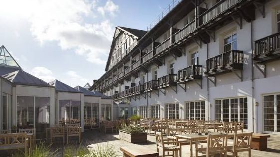 Billedet viser Marienlyst Strandhotel, hvor man ser den elegante hvide bygning med balkoner og en stor udendørs terrasse med træmøbler. Det ser det ud til, at der er gode udendørsforhold til teambuilding-aktiviteter.