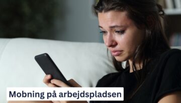 Billedet viser en grædende kvinde, der sidder med en smartphone i hånden og ser ud til at være dybt påvirket af noget, hun har læst eller modtaget. Nederst på billedet står teksten: "Mobning på arbejdspladsen."