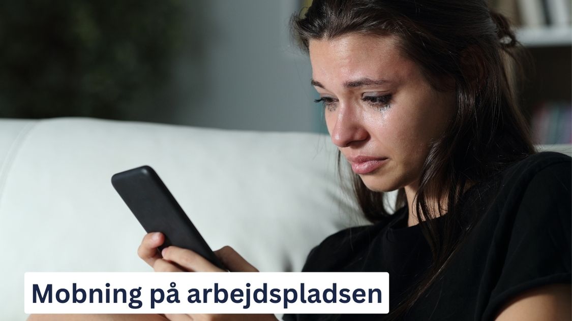 Billedet viser en grædende kvinde, der sidder med en smartphone i hånden og ser ud til at være dybt påvirket af noget, hun har læst eller modtaget. Nederst på billedet står teksten: "Mobning på arbejdspladsen."