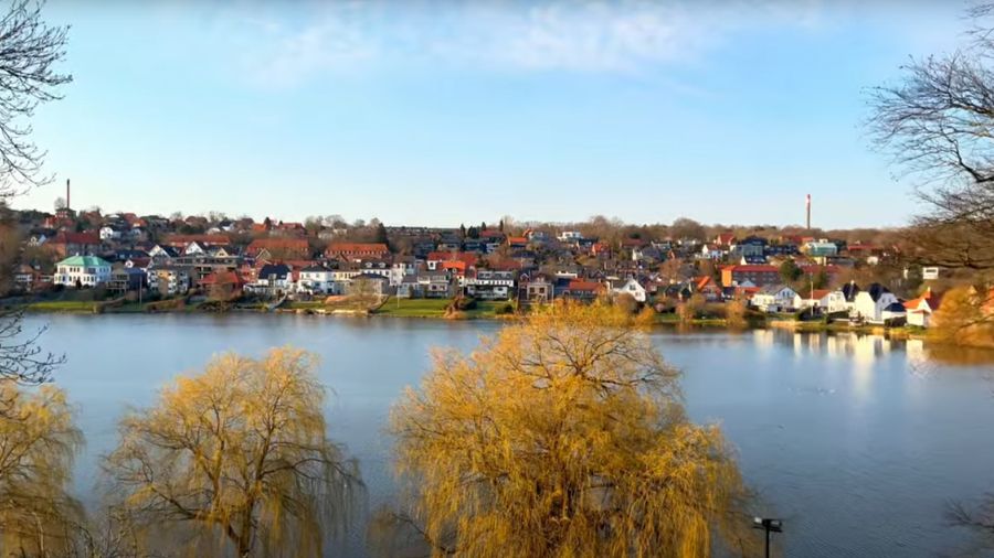 Dette billede viser en rolig udsigt over Kolding med byens huse og naturen omkring en sø. Den smukke natur og de fredelige omgivelser gør Kolding til et ideelt sted for firmaevents og teambuilding-aktiviteter, hvor man kan nyde både byens charme og de naturskønne omgivelser.